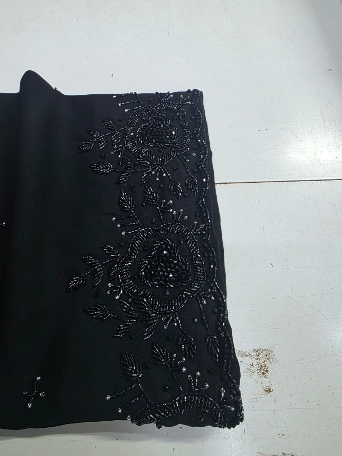 Black fabric with intricate beadwork on a white floor.